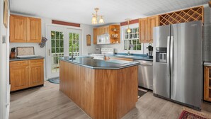 A kitchen with wooden cabinets, a central island, stainless steel appliances, and a view of greenery outside. - Twilight Cove: "Beautiful Sunset Views on Canandaigua Lake!" (Canandaigua)