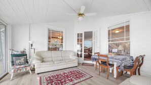A spacious room with a white sofa, a dining table with chairs, a ceiling fan, and large windows. - Twilight Cove: "Beautiful Sunset Views on Canandaigua Lake!" (Canandaigua)