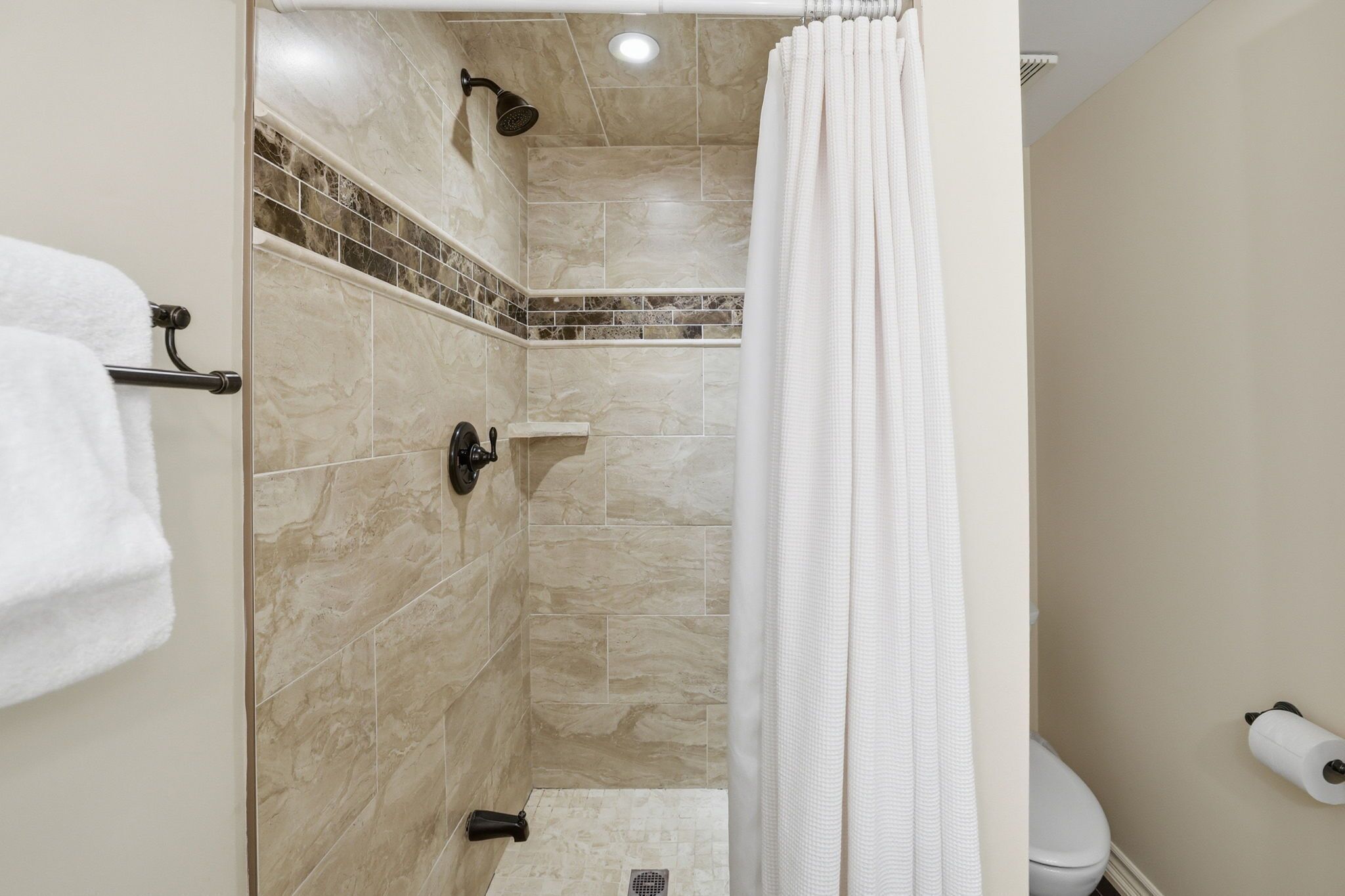 A shower with a glass door, a towel rack, and a toilet with a toilet paper holder.