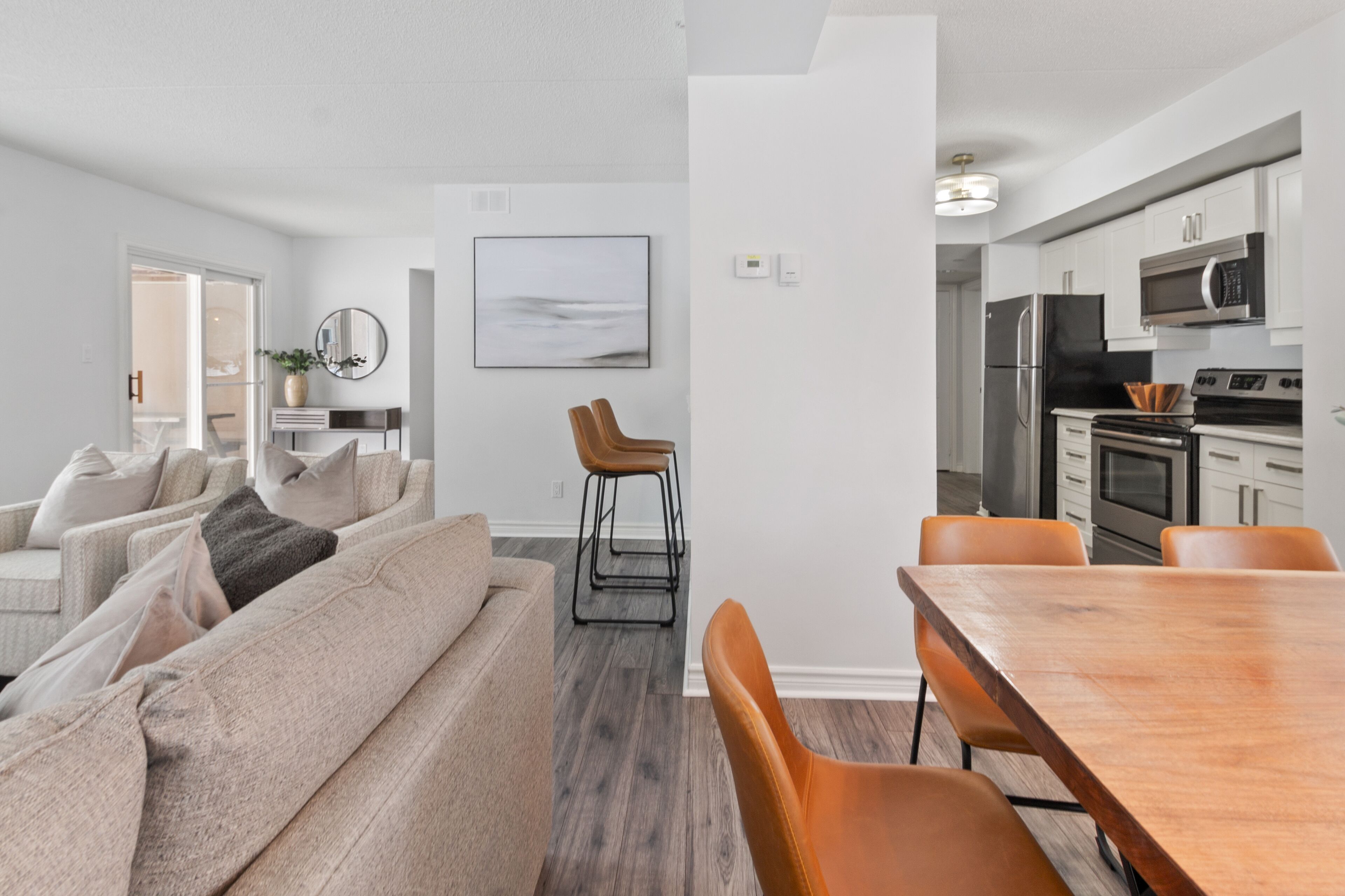 A modern kitchen with stainless steel appliances, a dining area with a wooden table and chairs, and a living room with a sofa and a coffee table.