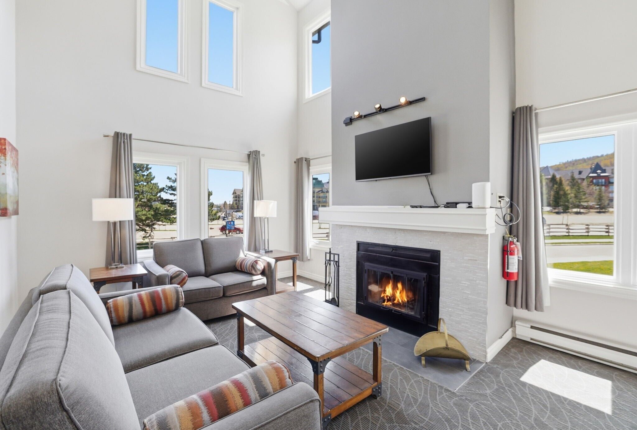 A modern living room with a fireplace, sofa, coffee table, and a flat-screen TV mounted on the wall.