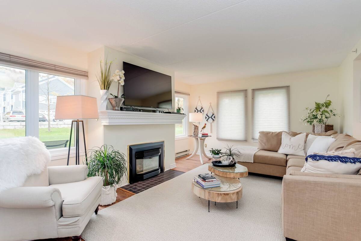 A modern living room with a fireplace, a sofa, a coffee table, and a television mounted above the fireplace.