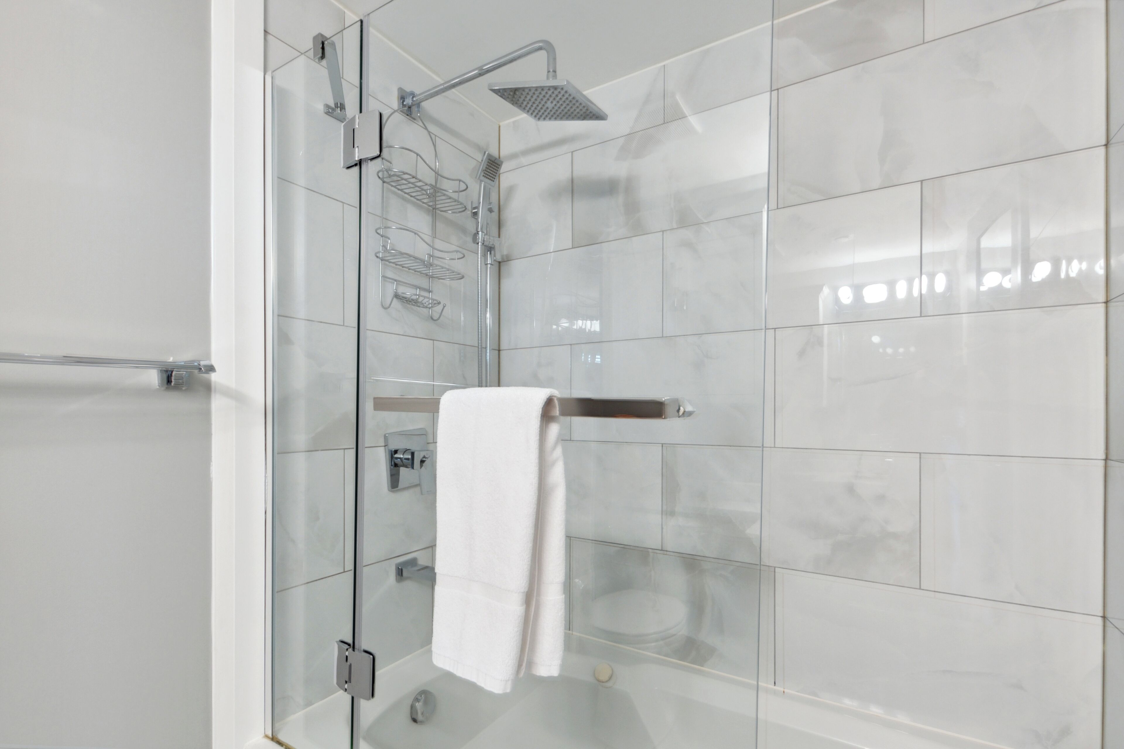 A modern bathroom with a glass shower enclosure, a white towel hanging on a metal rack, and a tiled wall.