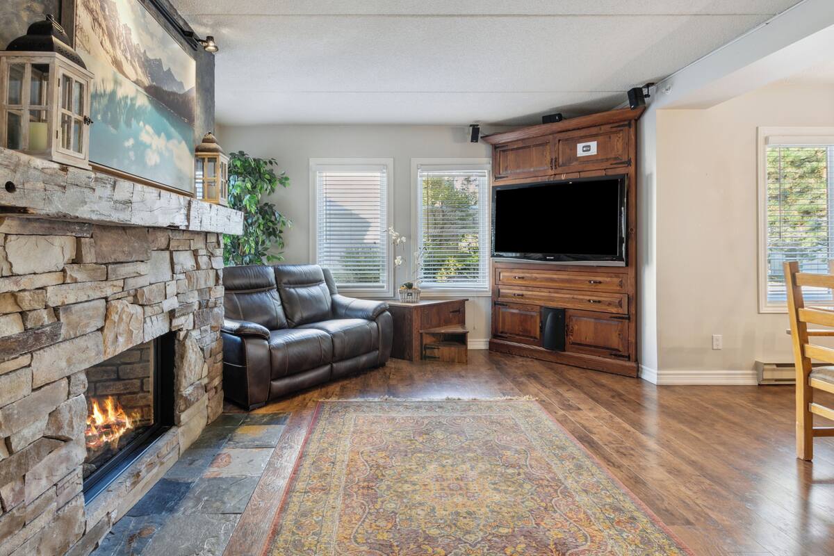 A living room with a stone fireplace, leather sofa, TV cabinet, and a patterned rug.