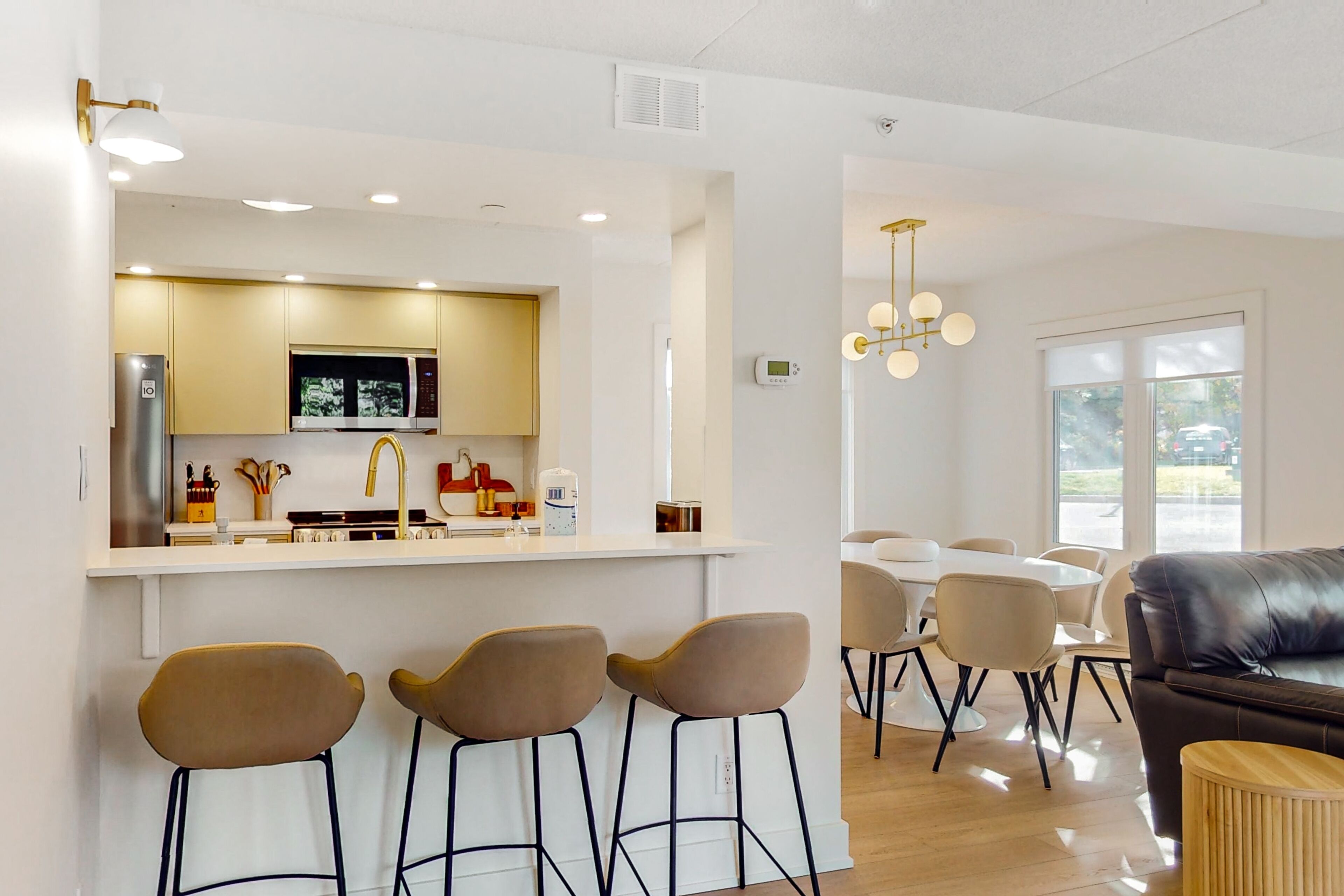 A modern kitchen with a central island, bar stools, and a dining area with a black leather couch and a round wooden side table.