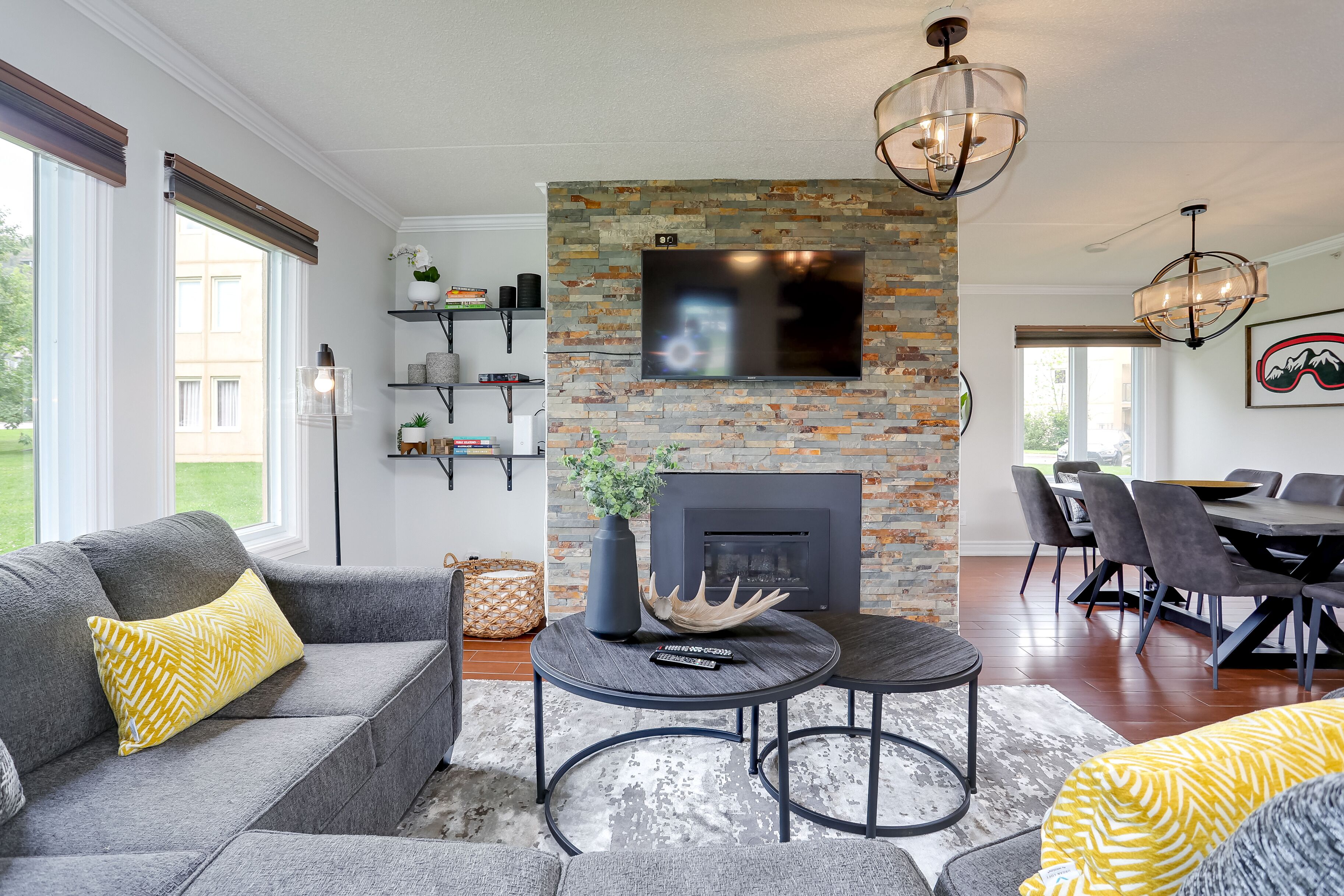 A modern living room with a fireplace, a flat-screen TV mounted on a brick wall, and a dining area with a table and chairs.