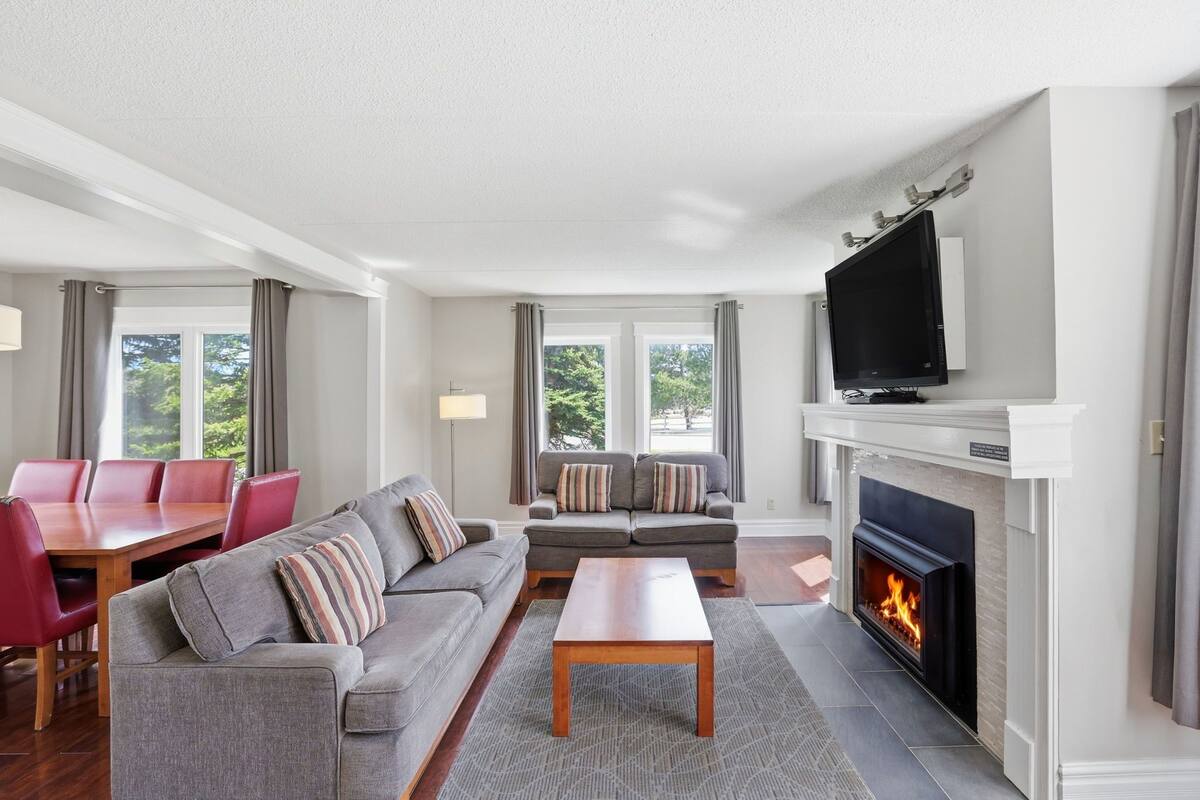 A modern living room with a fireplace, a television, a sofa set, and a dining area.