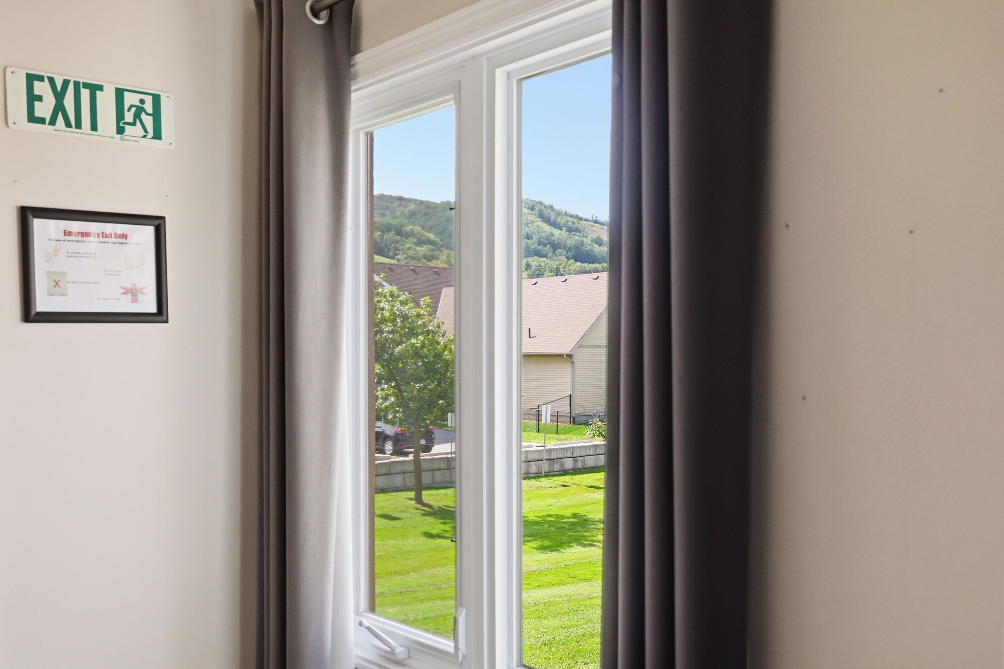 Una habitación con ventana, señal de salida y aviso de salida de emergencia enmarcado en la pared.