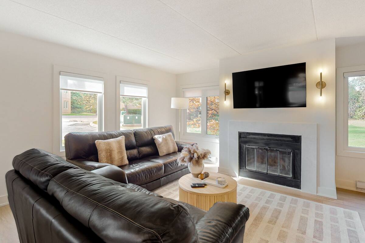 A modern living room with a black leather sofa, a fireplace, and a flat-screen TV mounted above it.