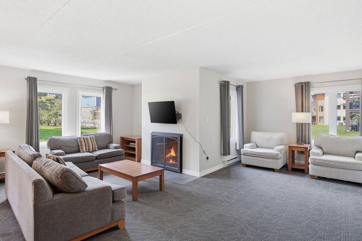 A modern living room with a fireplace, sofas, a coffee table, and a TV mounted on the wall.