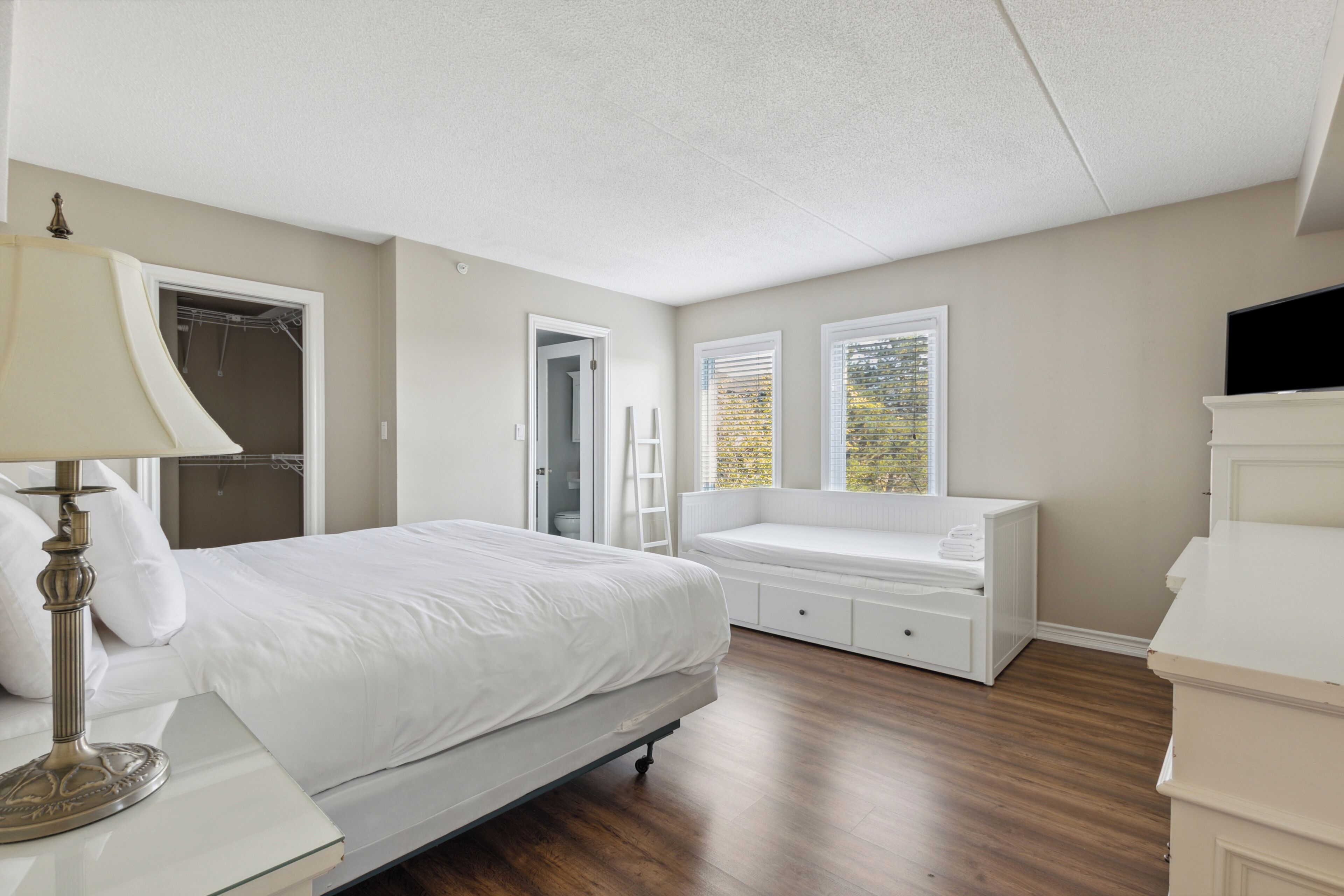 Ein Schlafzimmer mit Bett, Nachttisch, Lampe, Fensterbank und Fernseher.