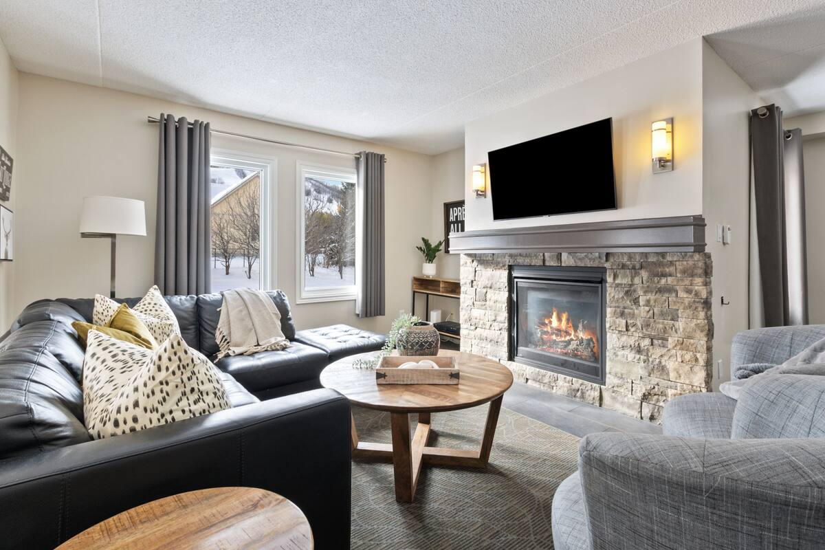 A modern living room with a fireplace, leather sofas, a flat-screen TV, and a stone accent wall.