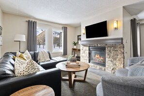 Una sala de estar moderna con chimenea, sofás de cuero, un televisor de pantalla plana y una pared de acento de piedra.