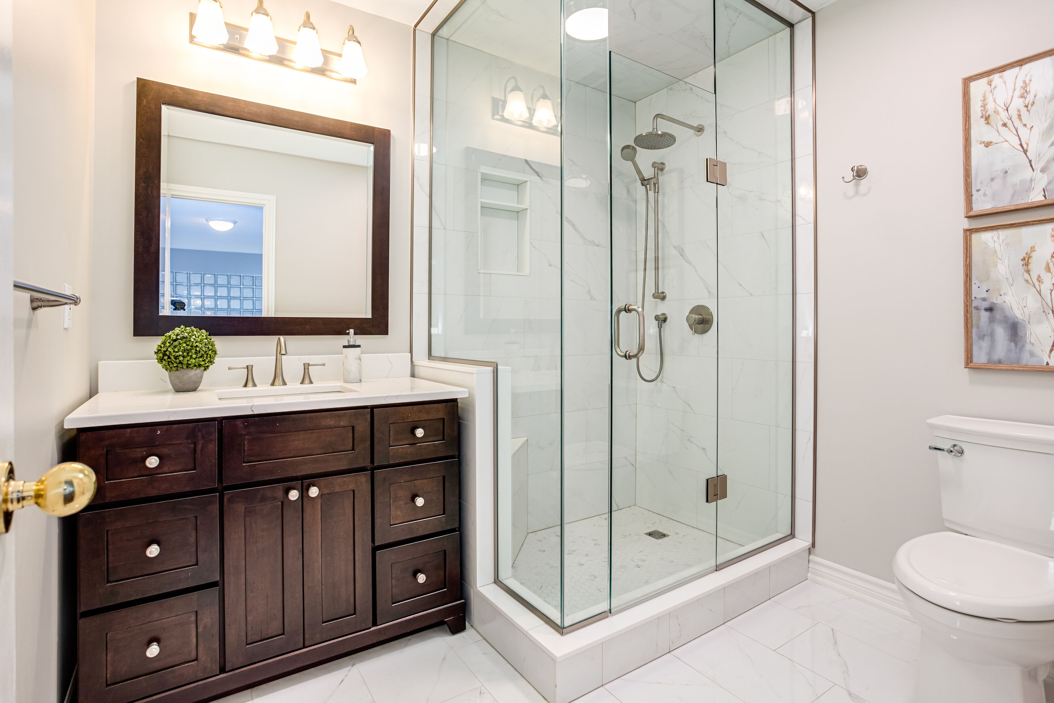 A modern bathroom with a glass-enclosed shower, a dark wood vanity, and a white toilet.