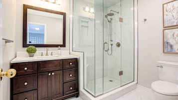 Une salle de bain moderne avec une douche à parois de verre, un meuble-lavabo en bois foncé et des toilettes blanches.