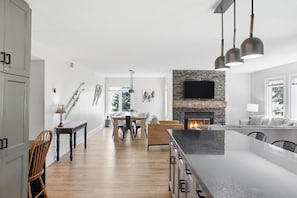 A modern kitchen with a stone fireplace, wooden dining table, and a large island with a black countertop.