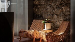 A room with a stone wall, wicker chairs, a potted plant, and a glass door.