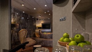 A modern living room with a sofa, chairs, and a TV. There are green apples and glasses on a table.