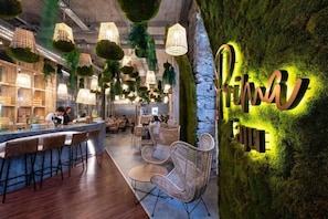 A modern restaurant interior with hanging green plants, wicker furniture, and a neon sign on the wall. - Caju Le Petit Hotel (Funchal)