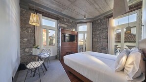 A bedroom with a large bed, stone walls, a TV, and a balcony with a view.