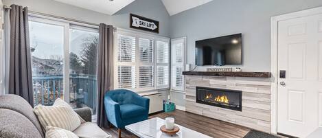 A living room with a sofa, a blue armchair, a fireplace, and a TV mounted on the wall.