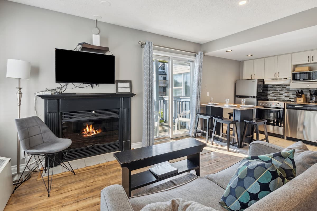 Una sala de estar moderna con chimenea, televisor y comedor, con una cocina al fondo.