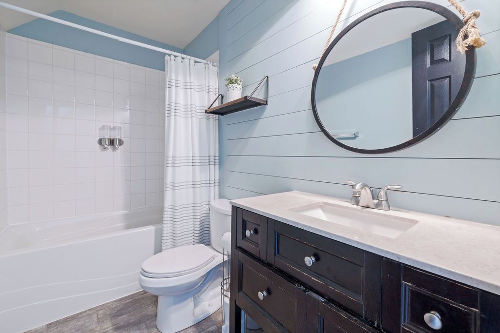 A bathroom with a bathtub, toilet, and vanity with a mirror and shelf.