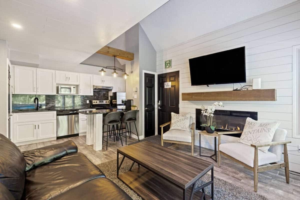 Una sala de estar moderna con chimenea, una cocina con armarios blancos y un comedor con mesa y sillas.