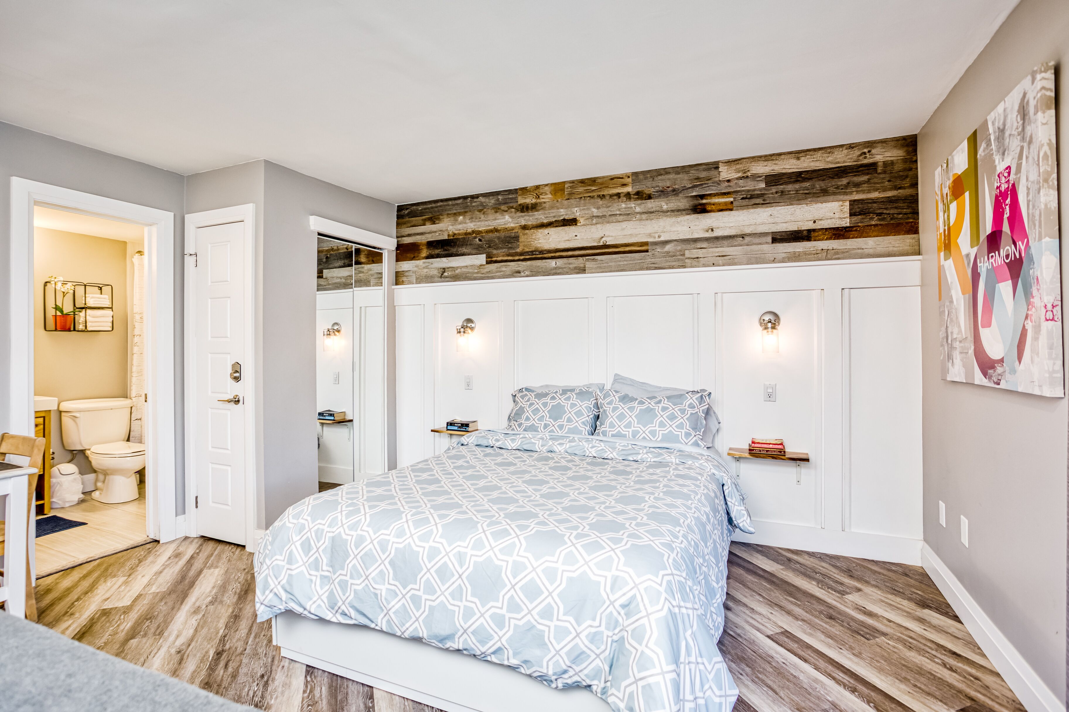 Un dormitorio con una cama grande, techo de madera, paredes blancas y un baño visible a través de una puerta abierta.