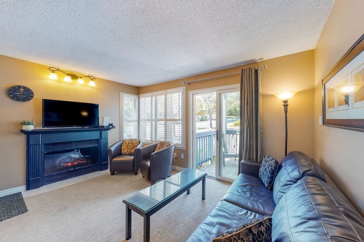 Una sala de estar con chimenea, un sofá, un televisor y un balcón con cortinas.