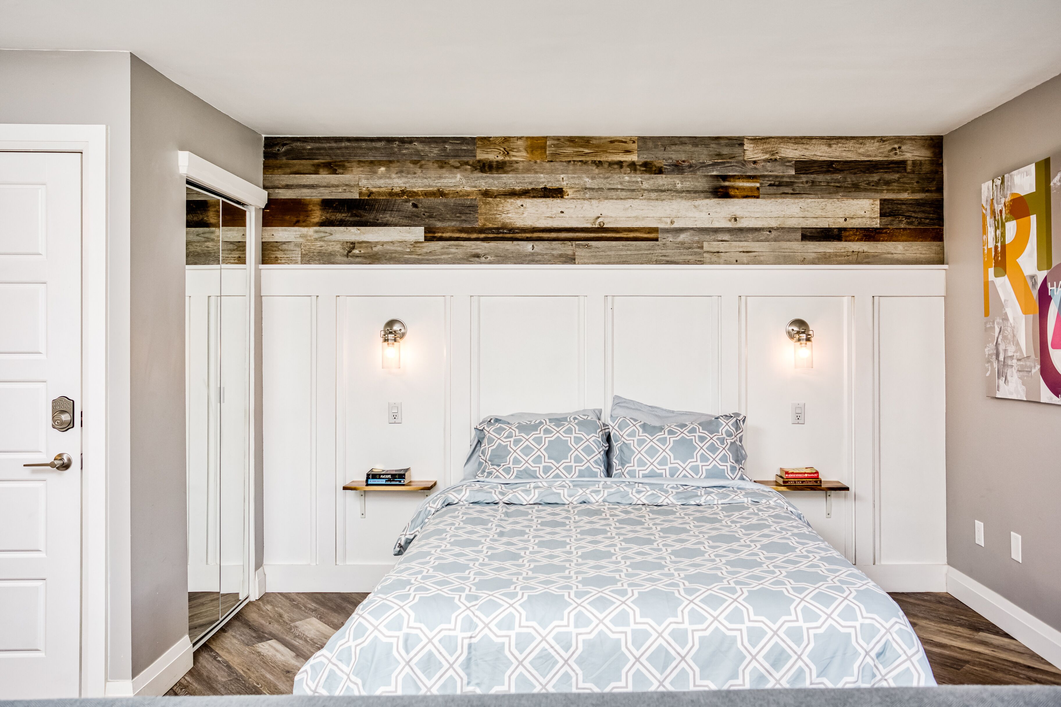 Um quarto com uma cama, duas mesas de cabeceira, uma parede de destaque em madeira e uma porta.