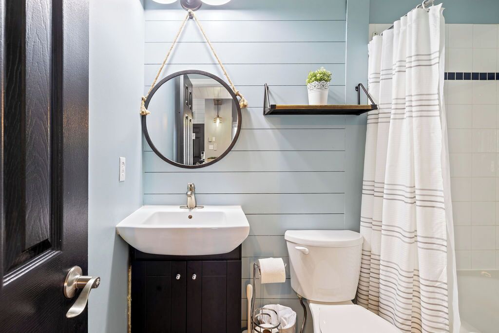 A bathroom with a white sink, dark cabinets, a toilet, a hanging mirror, and a shower curtain.