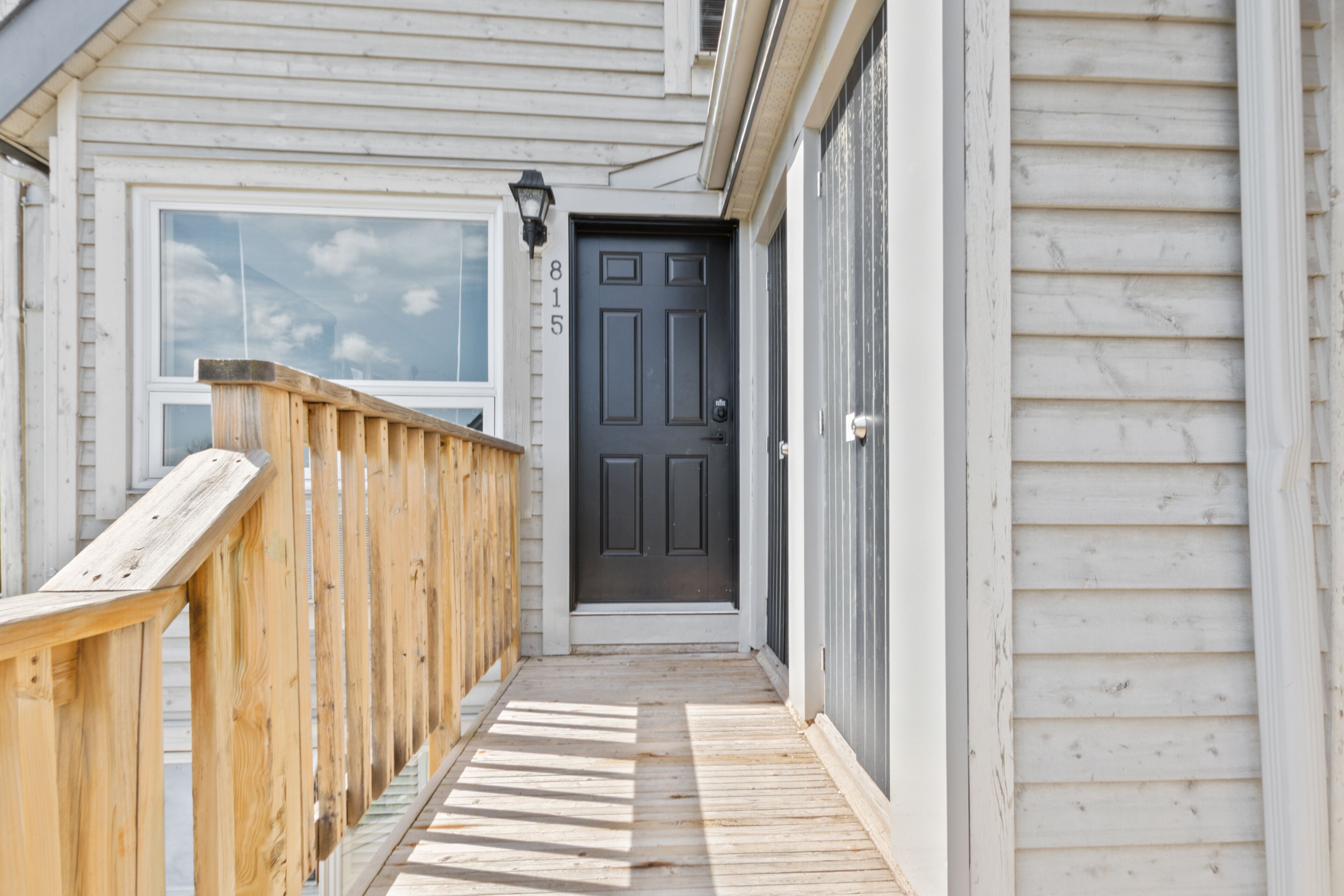 A wooden deck leading to a dark-colored door with the number 815 on the wall.