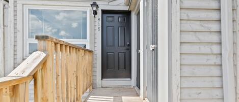 A wooden deck leading to a dark-colored door with the number 815 on the wall.