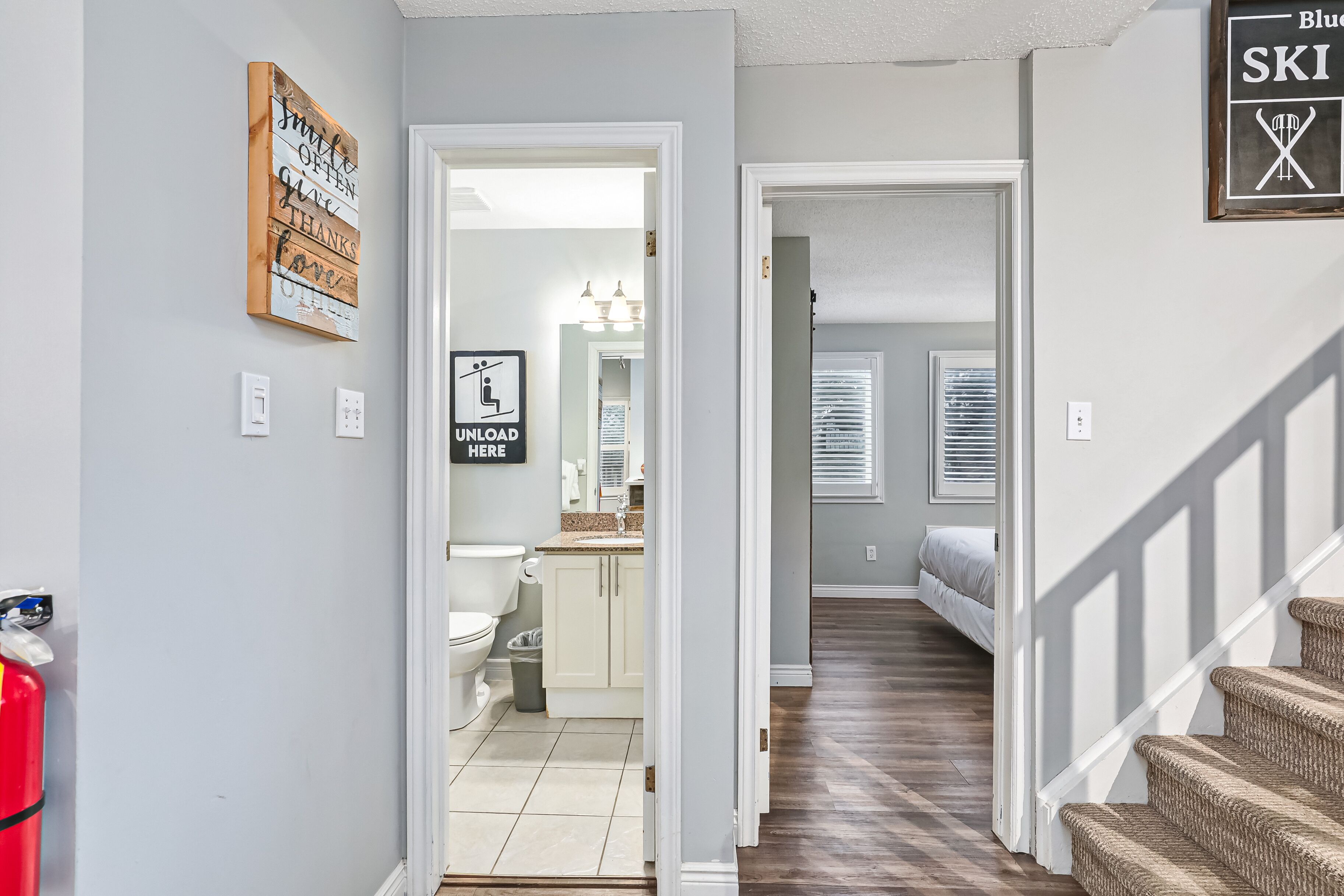 A hallway leading to a bathroom with a toilet, sink, and cabinet. There is a fire extinguisher on the left and a sign that says "UNLOAD MEKE".