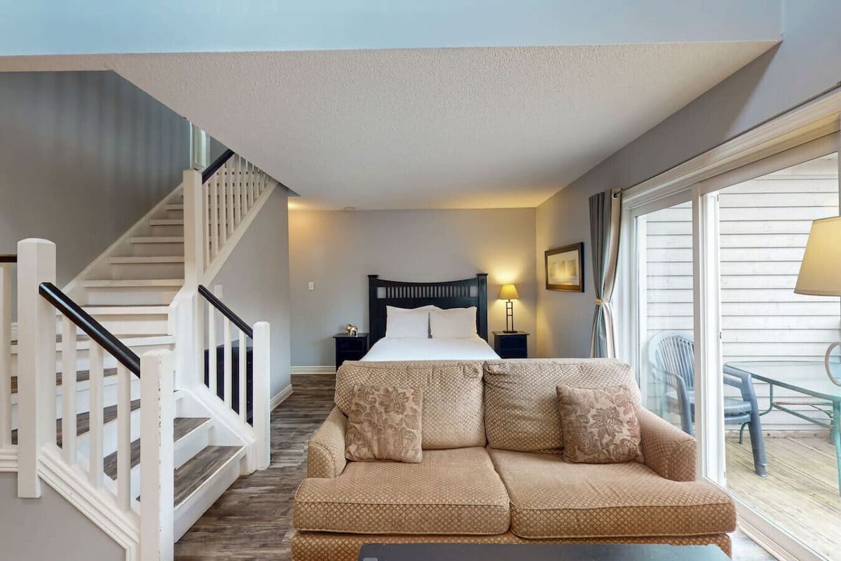 Un dormitorio con cama, sofá, escaleras, mesita de noche y ventana.