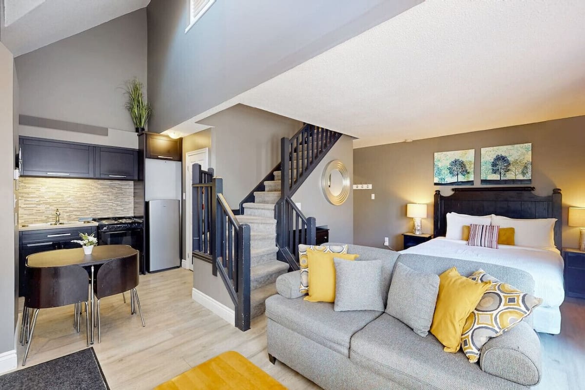 Un apartamento moderno con cocina, comedor, escaleras y un dormitorio con cama y mesitas de noche.
