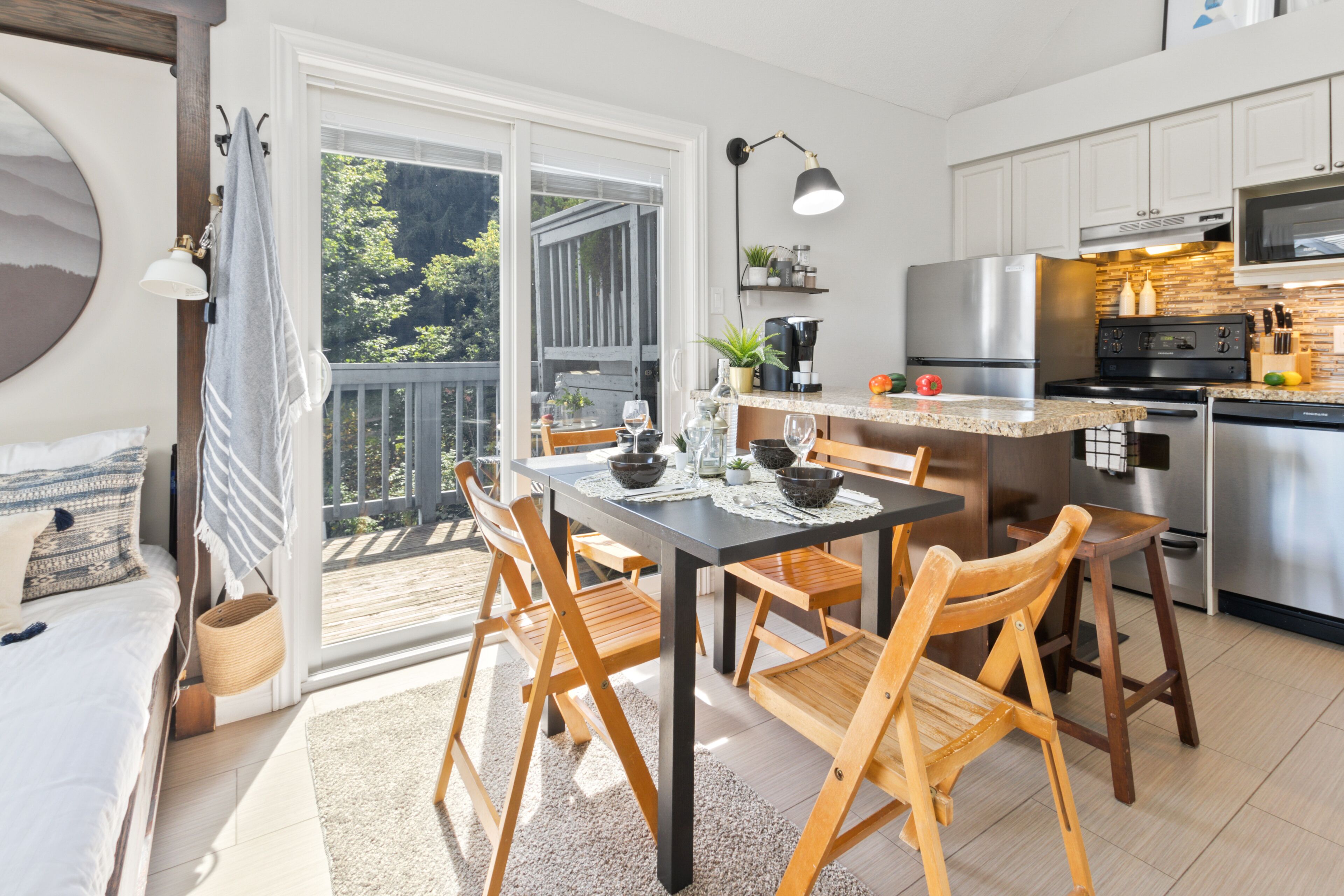 A modern kitchen with a dining area, large windows, and a view of the outdoors.