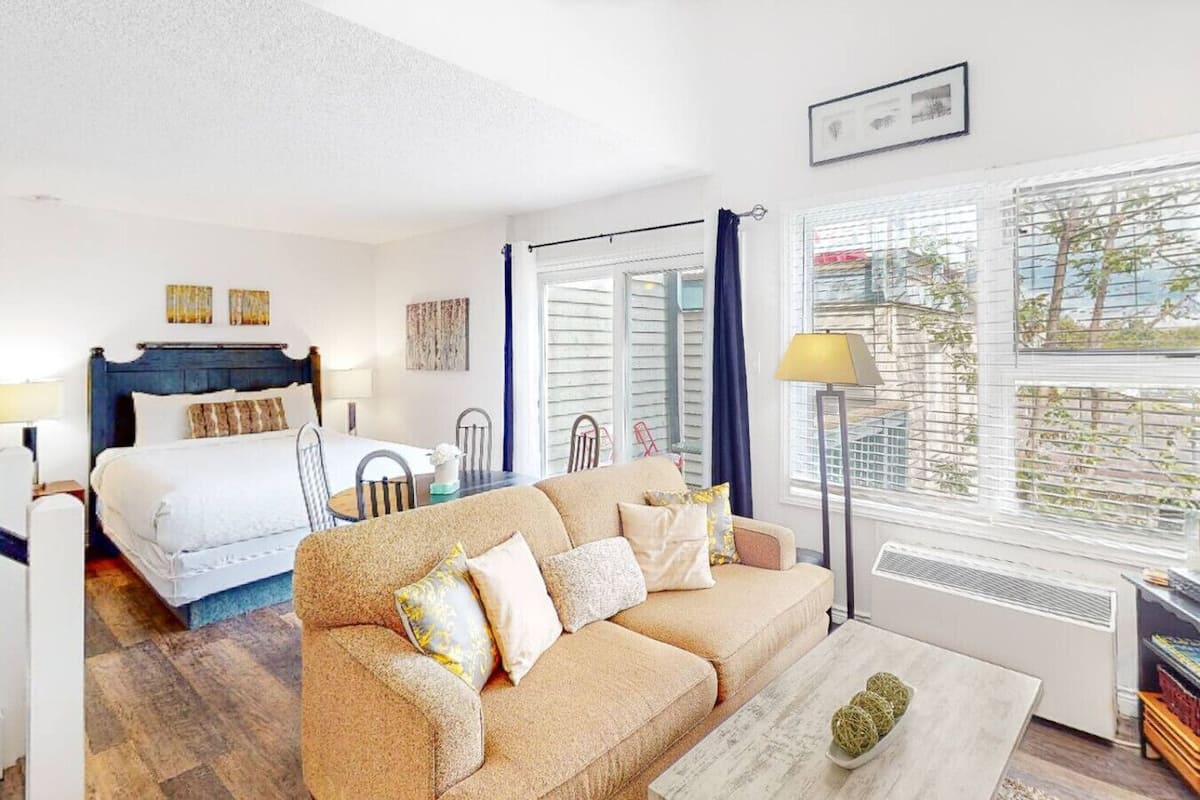 Una habitación de hotel con cama, sofá, mesa de comedor y un ventanal con persianas.