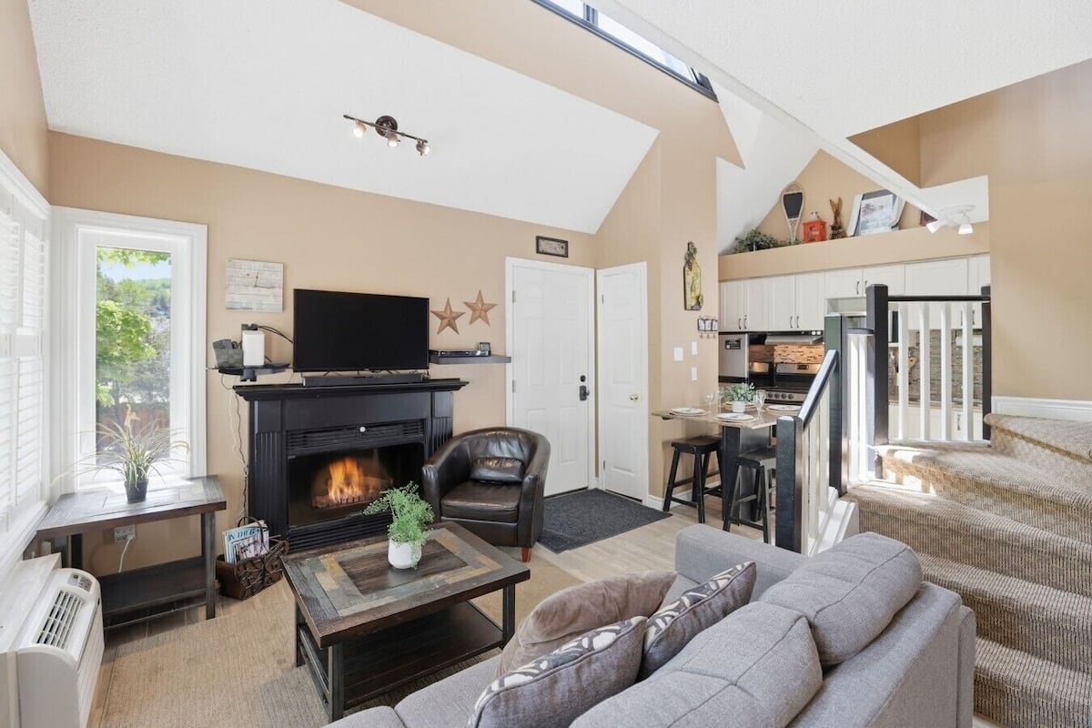 Una sala de estar con chimenea, un sofá, un televisor y una zona de cocina.