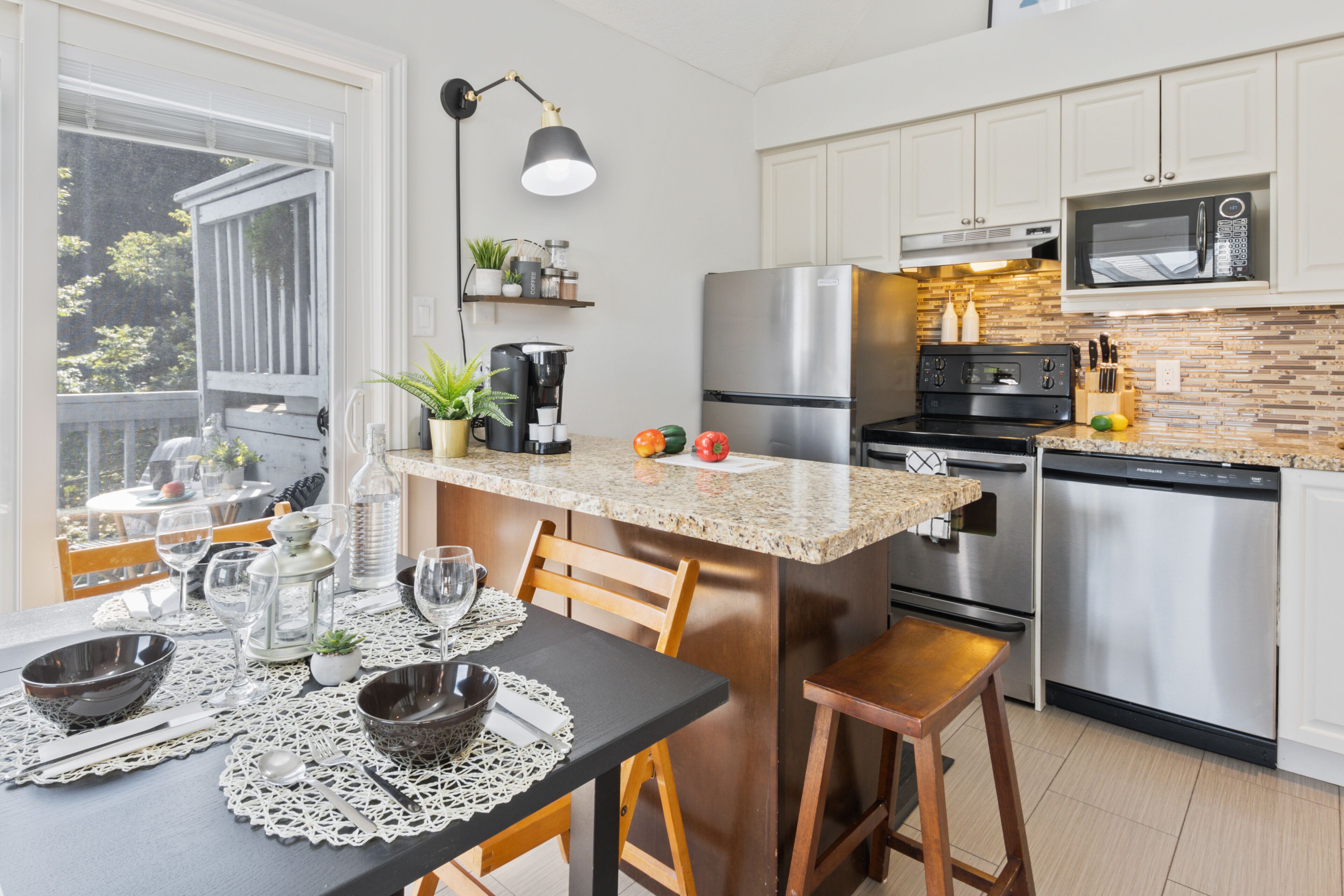 Uma cozinha moderna com bancada de granito, eletrodomésticos de aço inoxidável e uma área de jantar com mesa posta para dois.