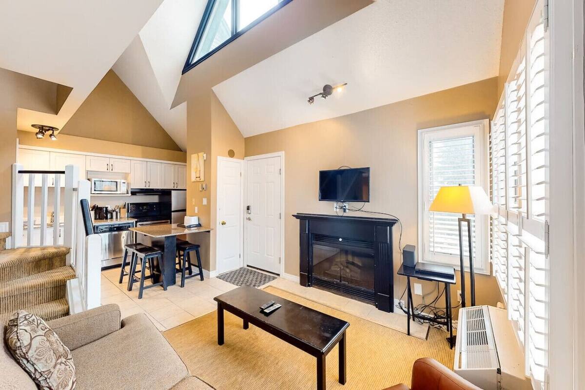 Una sala de estar con chimenea, televisor y comedor, con una cocina al fondo.
