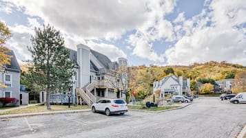 A residential street with houses, a white SUV parked on the side, and autumn foliage in the background.