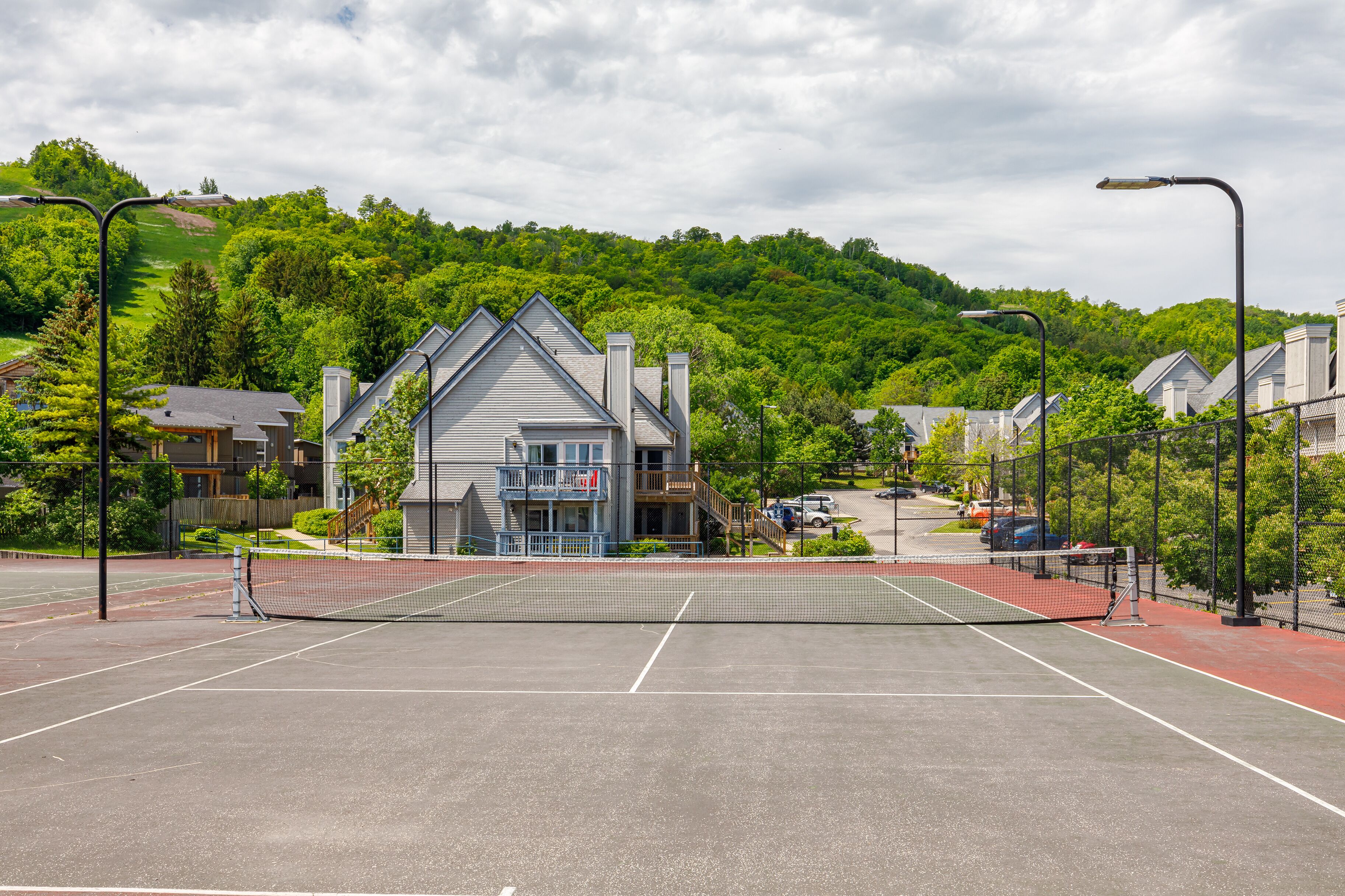 A tennis court with a net, surrounded by a fence, and a building with a balcony in the background.