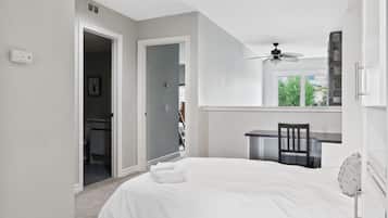 A bedroom with a bed, a desk, and a chair. There is a door leading to another room.