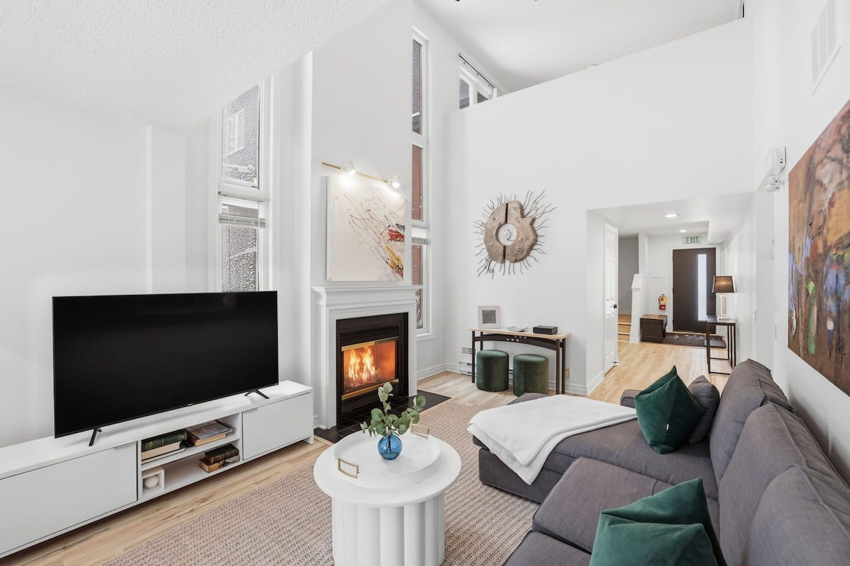 A modern living room with a flat-screen TV, fireplace, sofa, and artwork.