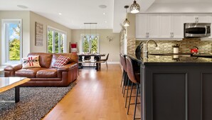 A spacious living area with a leather sofa, dining table, and kitchen with white cabinets and a large island. - Sierra Lane Condos (The Blue Mountains)