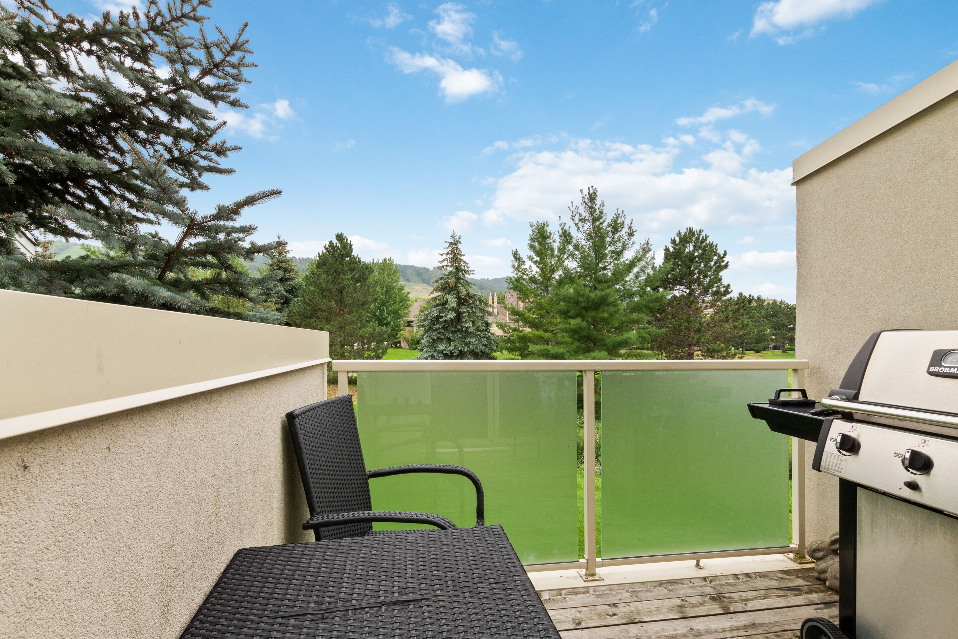 Ein Balkon mit Grill, Stuhl und Blick auf Bäume und Hügel.