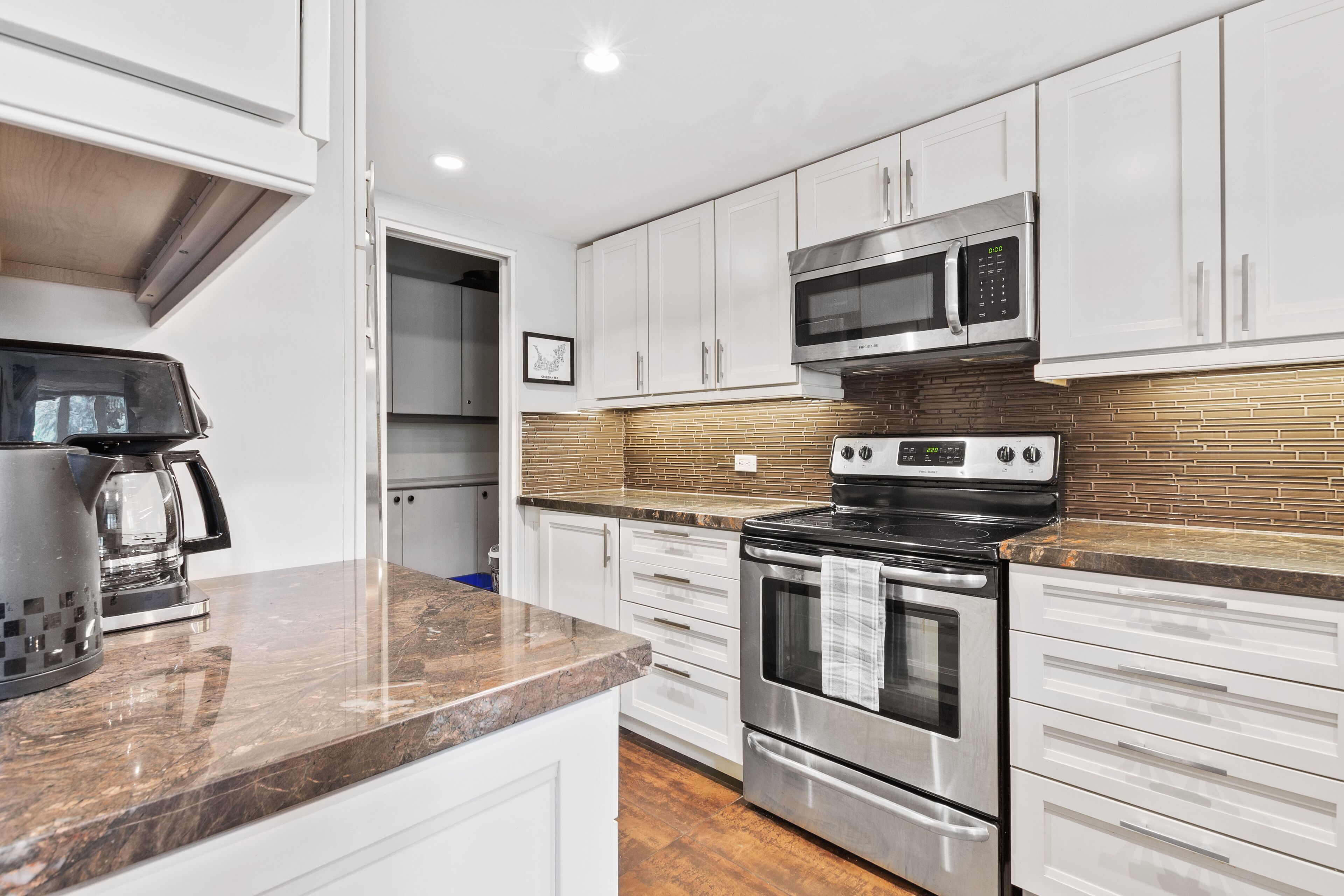 A modern kitchen with white cabinets, a stainless steel microwave, an oven, and a coffee maker on the countertop.