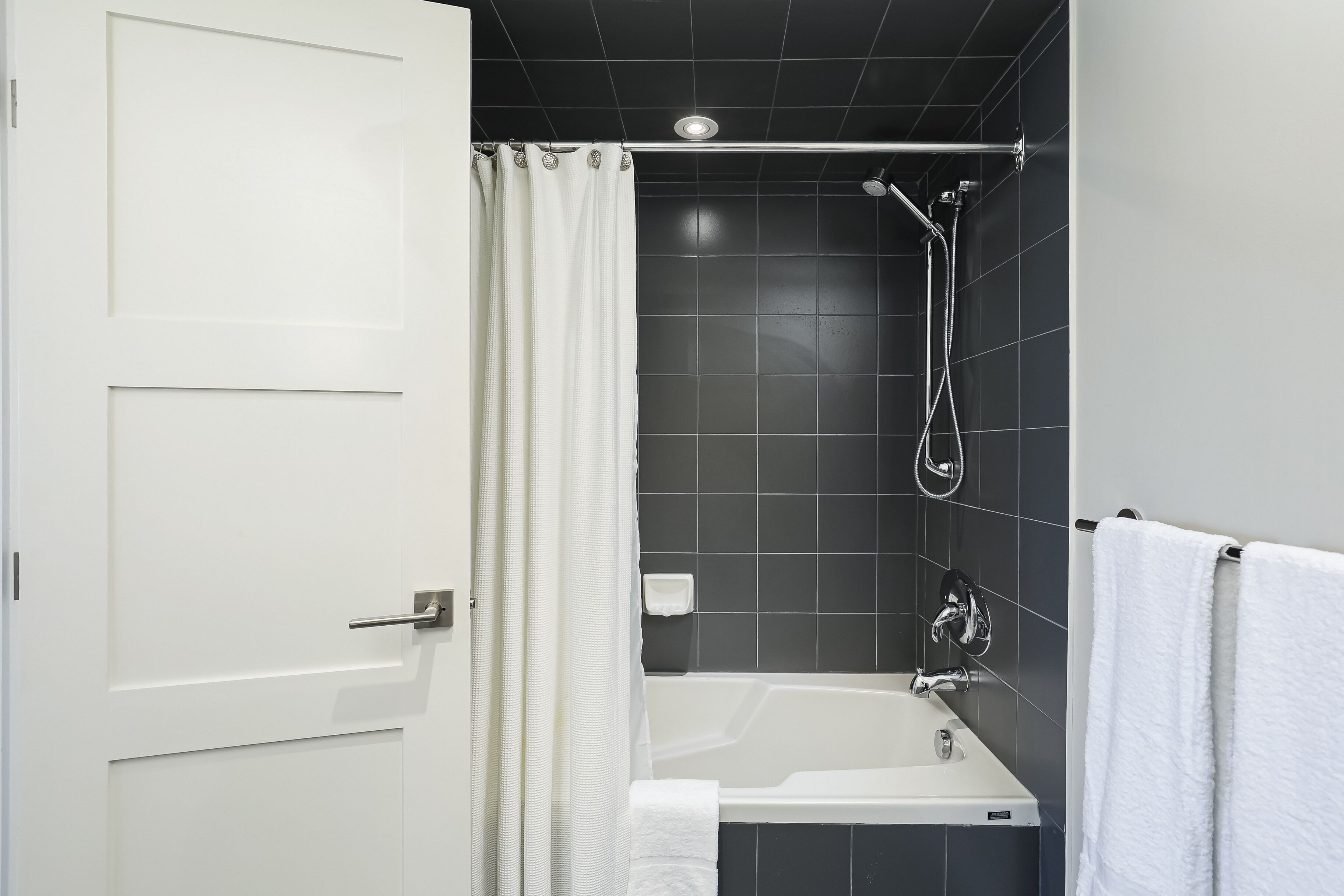 Een moderne badkamer met een bad, douche en een witte deur.